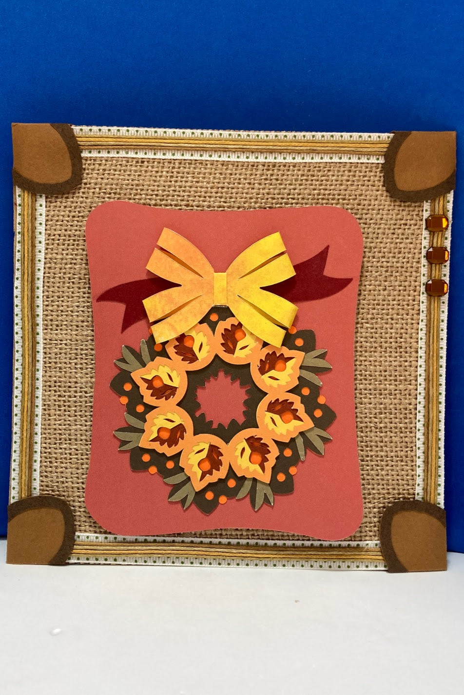 Handcrafted autumn decorative square featuring a layered wreath and yellow bow on burlap-style paper.