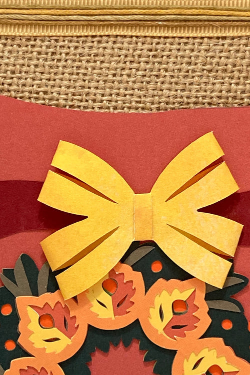 Close-up of the autumn wreath design with a yellow bow and layered leaves.